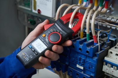 Electrician with measurere of electrical paramenters with tester multimeter equipment at electrical fusebox or switch box