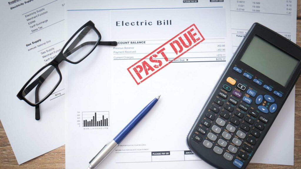 An electric bill stamped past due, with reading glasses and a calculator