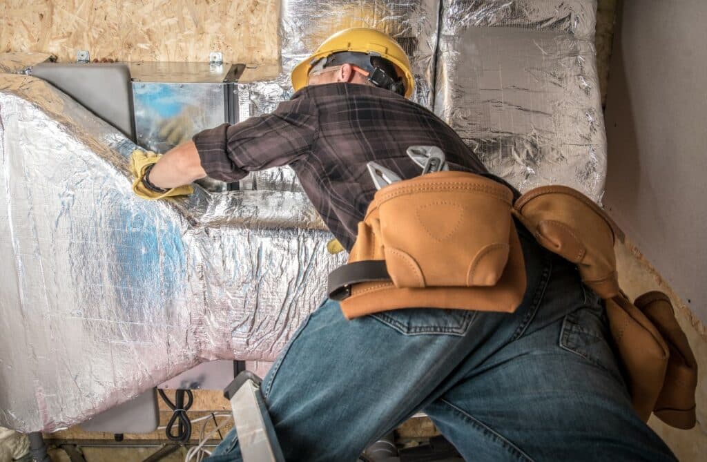 Worker in Yellow Hard Hat Installing Furnace and Central Heating Pump Duct. Heating and Cooling Work.