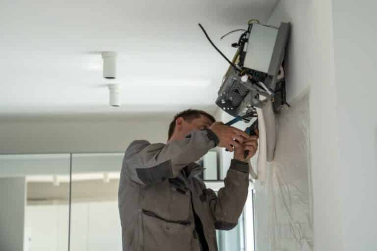 Fan cleaner and maintenance specialist installs on wall air conditioner at home for fresh cooling. Fan cleaner and maintenance specialist installs air conditioner at home for fresh cooling. Man in uniform make ventilation system control cool or heat air for comfort. Master for difficult home works.
