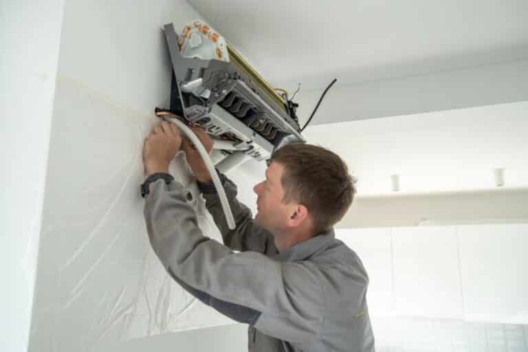 Installing air conditioner in house. Man specialist wearing work uniform fixing air cooler system. Installing air conditioner in house. Man technician specialist wearing work uniform fixing air cooler system on wall. Fan cleaning and maintenance specialist replaces filters for fresh air at home.