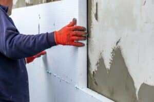 Construction worker installing styrofoam insulation sheets on house facade wall for thermal protection.
